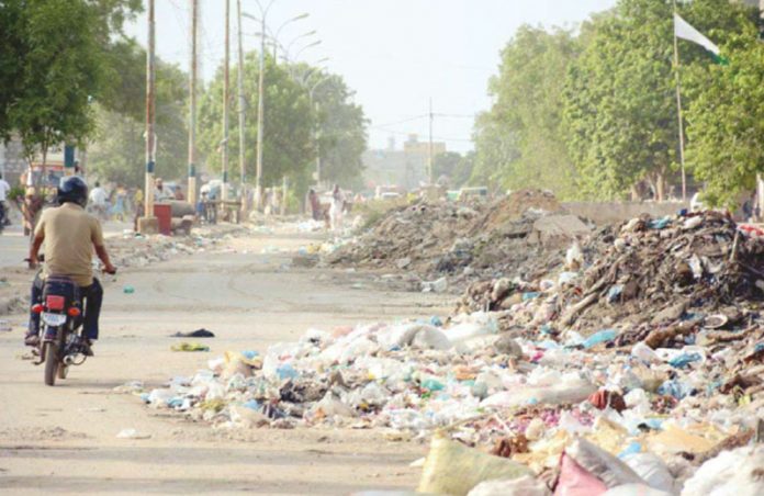 کراچی کے علاقے کورنگی میں ایک سٹرک پر کچرے کے ڈھیر لگے ہیں جس کے باعث گاڑیوں کا گزرنا تقریباً ناممکن ہے